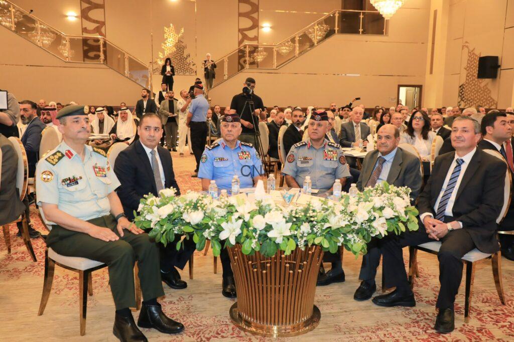 Group of officials and military officers seated at a formal ceremony around a flower-adorned table in a grand hall.