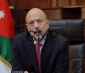 razaz - Center News Network Bald, bearded man in a dark suit speaking from a desk in a formal setting, with a flag in the background.