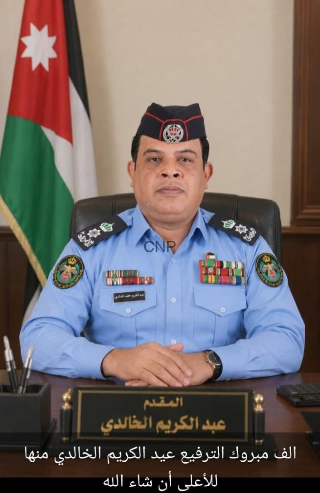 Portrait of a Jordanian police officer in a blue uniform with medals, seated at a desk with a Jordanian flag in the background.