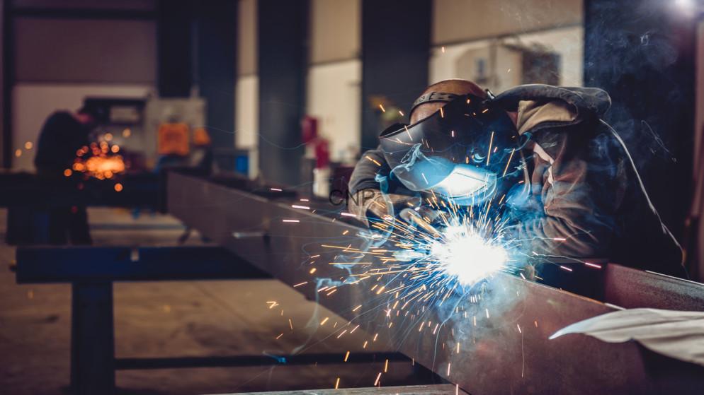sena - Center News Network Welder in protective gear arc-welding a steel beam in a workshop, sparks flying around the bright arc.