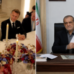 Two men in suits sign a document at a formal signing table with candles and a flower centerpiece on the table.