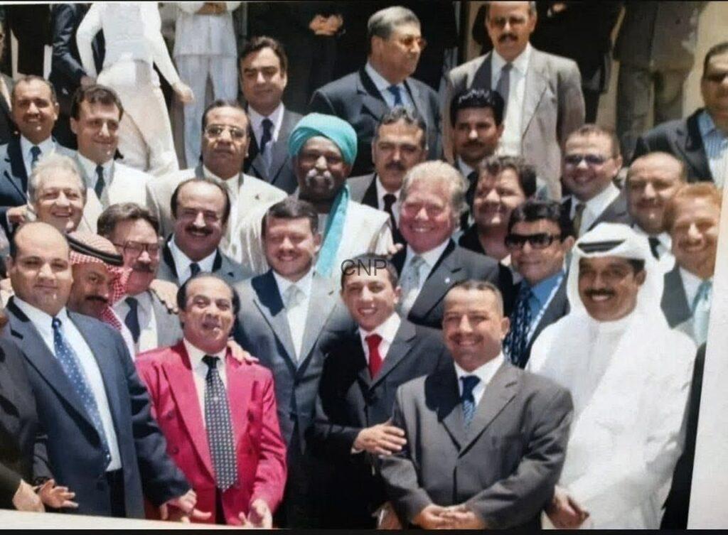 Large group of men in suits and traditional attire posing for a group photo on steps outdoors.