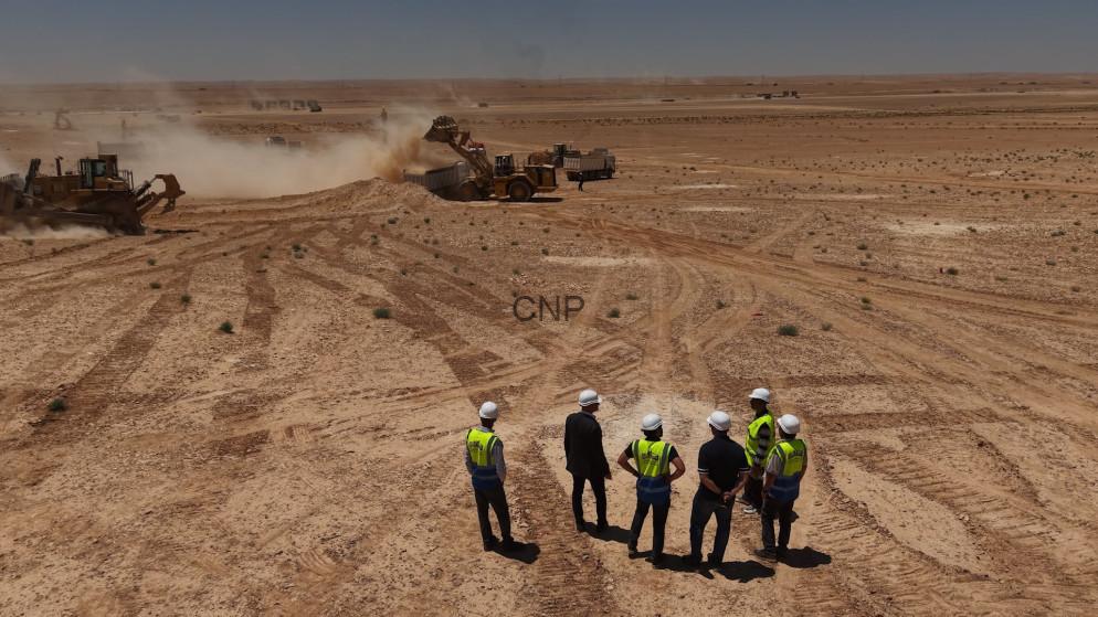 stad - Center News Network Construction crew in hard hats and neon vests observe desert earthworks as heavy machinery dig and move soil in a dusty excavation site.
