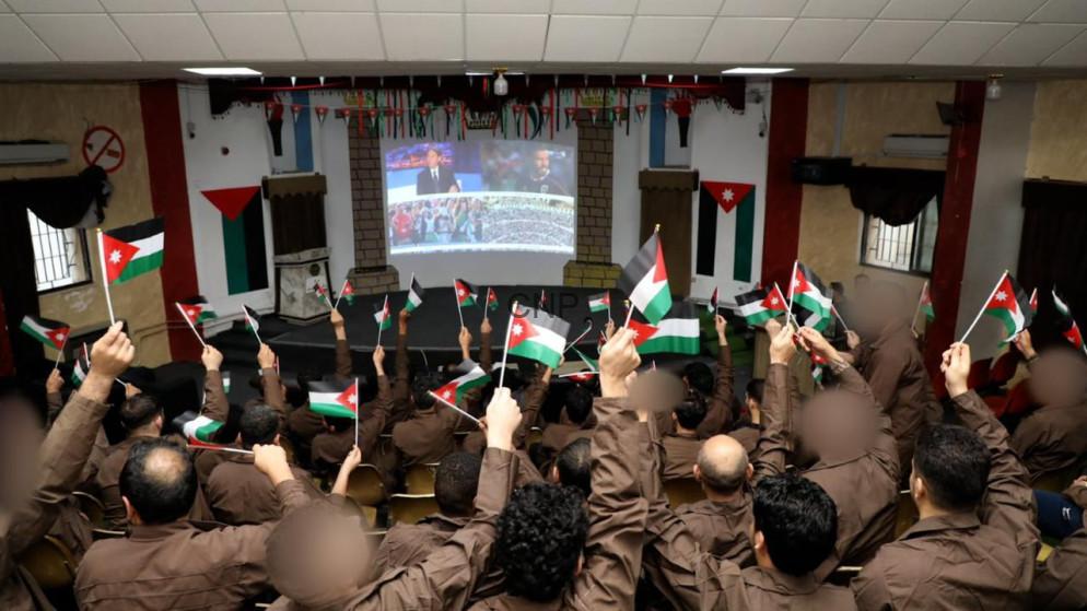 swaqa - Center News Network Audience in brown uniforms waving Palestinian flags while watching a broadcast on a large screen in a decorated hall with flags on the walls and ceiling.