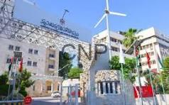 Entrance to a campus or corporate complex featuring a curved stone gate with a large sign, a wind turbine in the background, and a beige multi-story building under a clear blue sky.