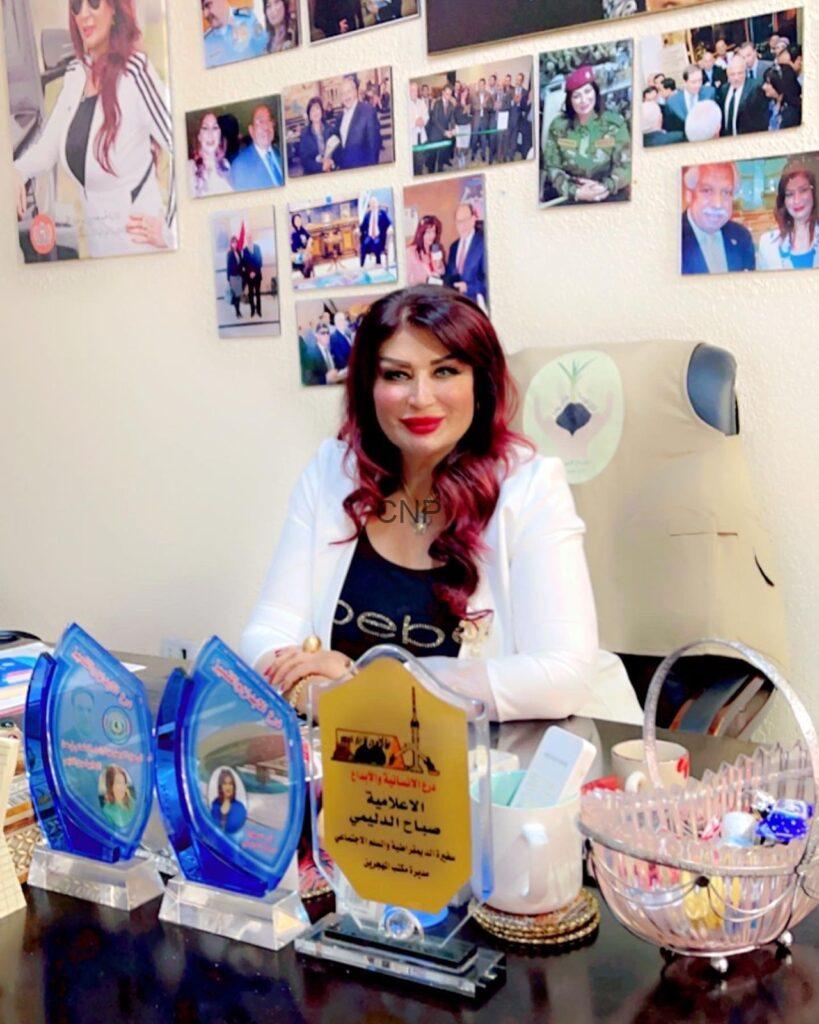 whs - Center News Network Smiling woman in a white blazer sits at a desk displaying multiple blue trophy plaques; wall behind her is covered with photo collages and awards photos.