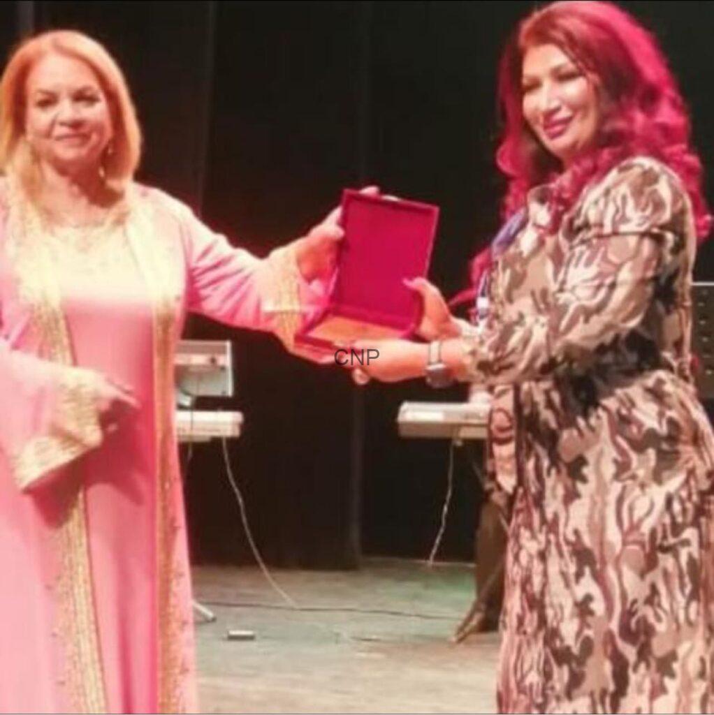 wsh - Center News Network Two women on a stage exchange an open red award box during a ceremony, both smiling.