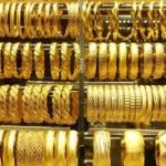Stacked shelves of gold bangles and bracelets in a jewelry shop display case, varying in width and designs.