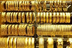 Stacked shelves of gold bangles and bracelets in a jewelry shop display case, varying in width and designs.