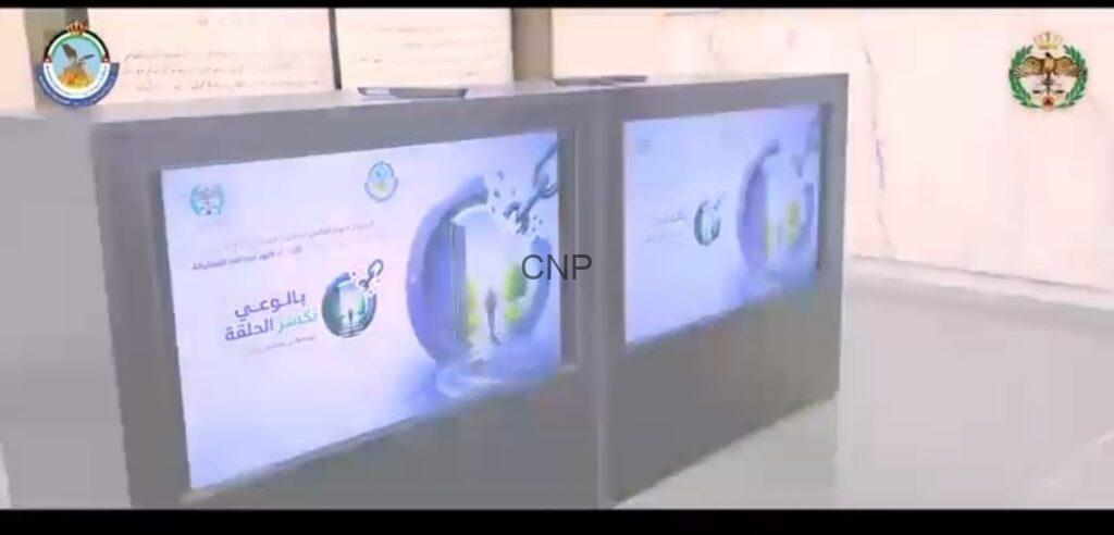 Two large display screens with Arabic banners and logos, set in a bright indoor space (likely an exhibit or presentation area).