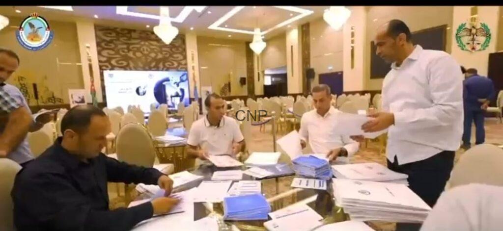 bb5 - Center News Network Group of men seated around a round table in a banquet hall, sorting and stamping stacks of papers during an event registration or briefing.