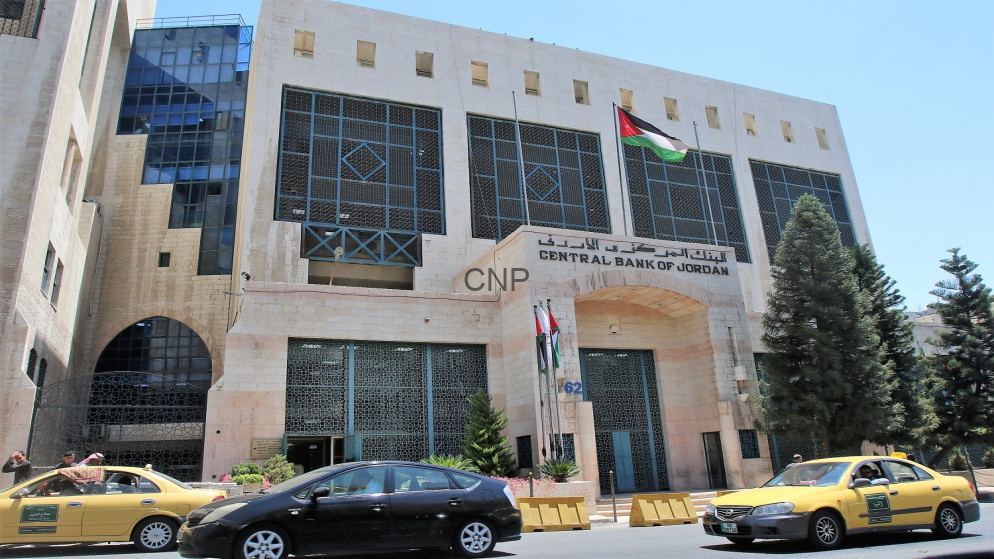 image - Center News Network Facade of the Central Bank of Jordan building with a Jordanian flag above the entrance and cars on the street in front.