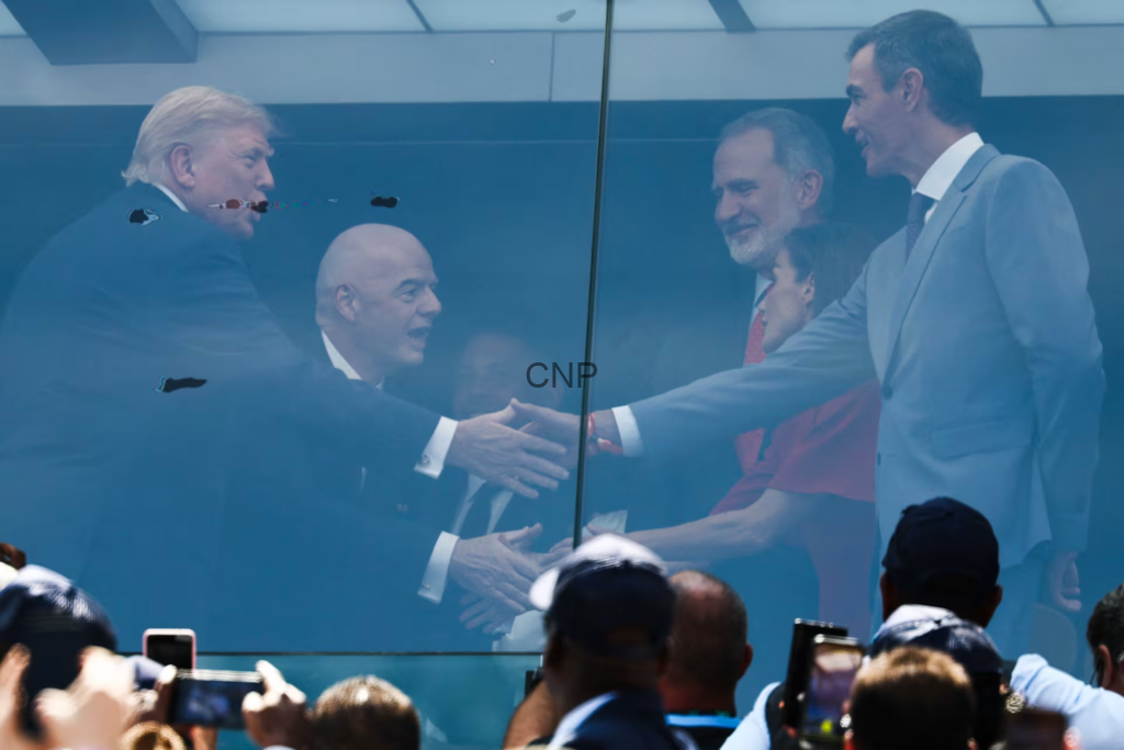 image - Center News Network Business leaders shake hands through a glass partition at a public event, with a cheering crowd taking photos in the foreground.