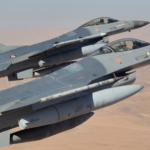 Two two-seat fighter jets in formation flying over a desert, armed with missiles under their wings