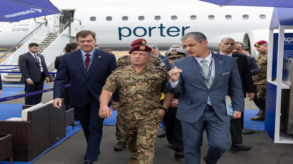 image - Center News Network VIP delegation walks on an airport tarmac beside a Porter Airlines plane, led by a camo-clad military officer and two men in suits behind him.