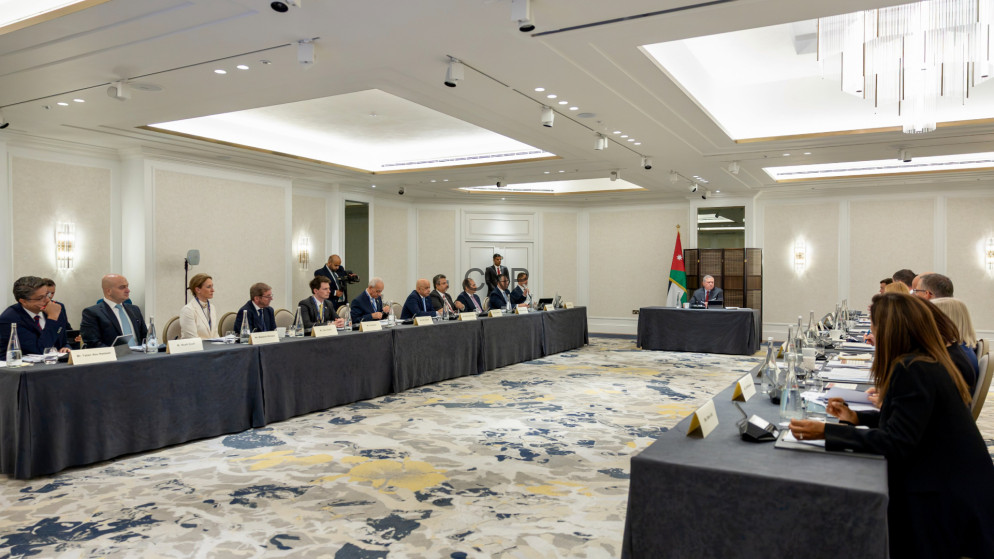 Formal diplomatic meeting in a bright hotel ballroom; delegates sit along two long tables facing each other, Jordan flag at the head table.