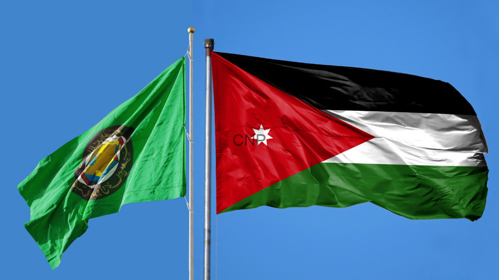 image - Center News Network Two flags flying on flagpoles against a clear blue sky: a green flag with a circular emblem on the left and the Jordan flag on the right, with black, white, green stripes and a red triangle.