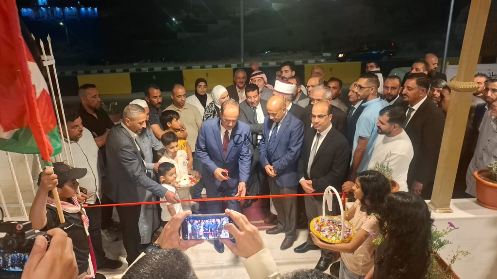 image - Center News Network Officials in suits cutting a red ribbon at an outdoor opening ceremony, surrounded by onlookers and photographers, with children and a woman holding a decorative basket nearby.