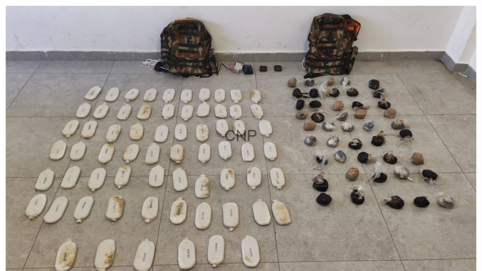 image - Center News Network Law enforcement drug seizure: numerous white brick-shaped packages laid out in neat rows on a tiled floor, with two camouflage backpacks above and smaller bags to the right.