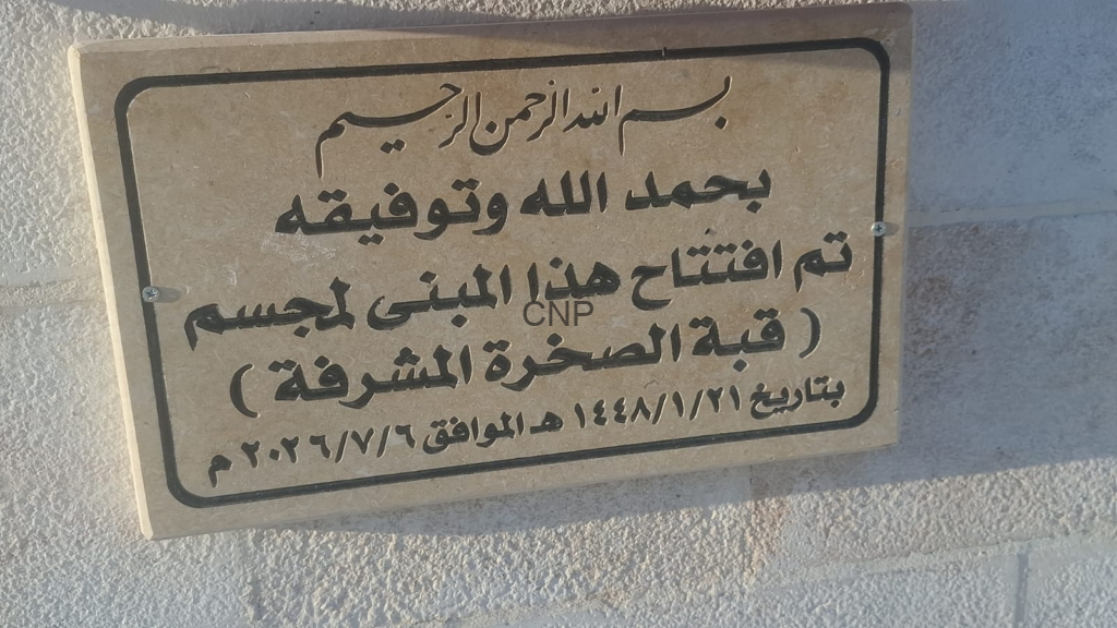 Commemorative stone plaque with Arabic inscription about the opening of this building, mounted on a textured white wall.