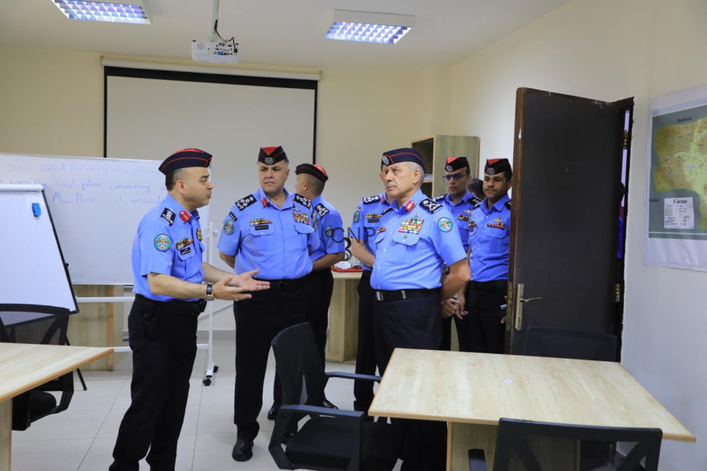 image - Center News Network Group of police officers in blue uniforms and red berets standing in a classroom, one officer speaking as others listen.