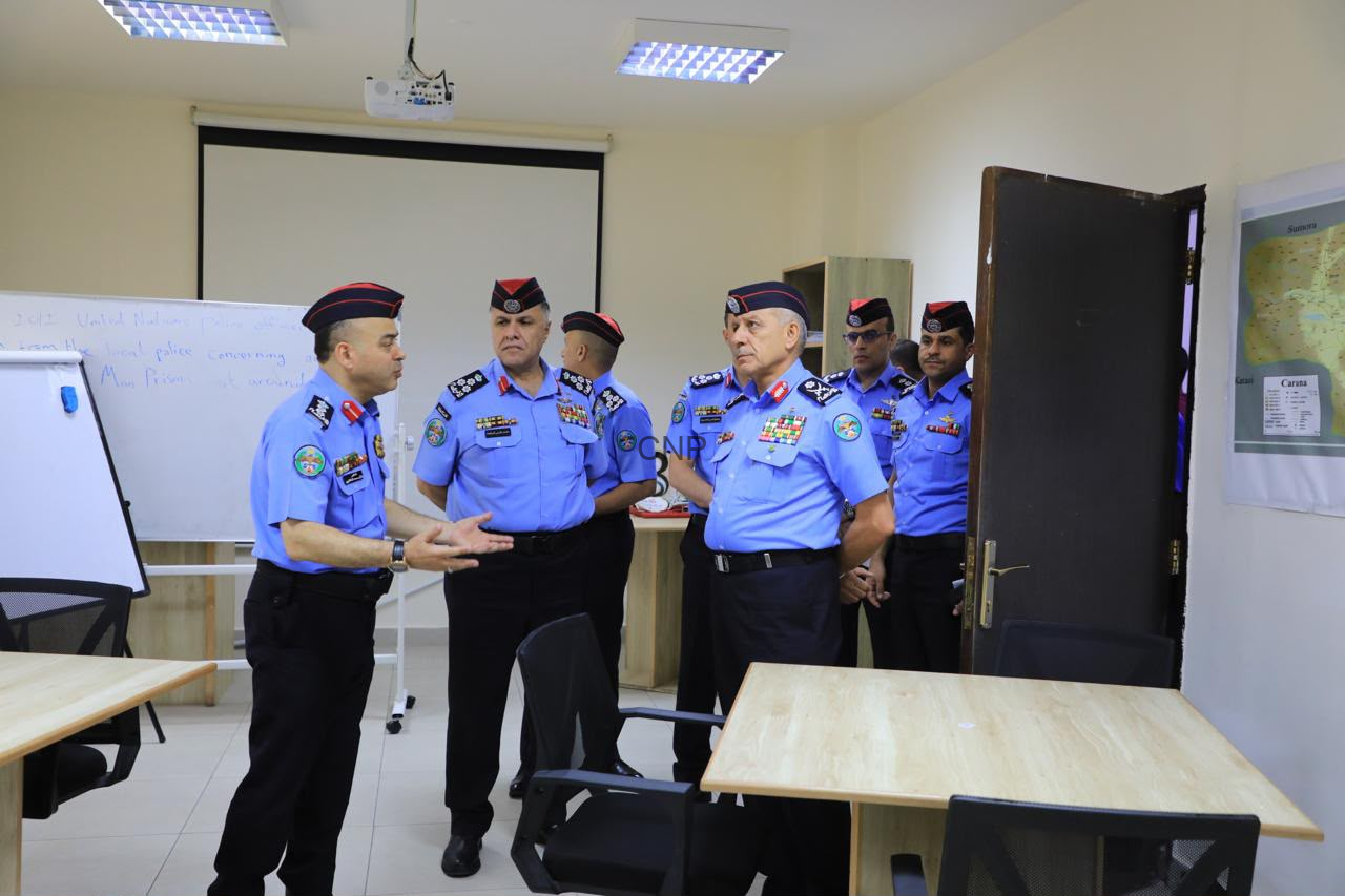 image - Center News Network Group of police officers in blue uniforms and red berets standing in a classroom, one officer speaking as others listen.