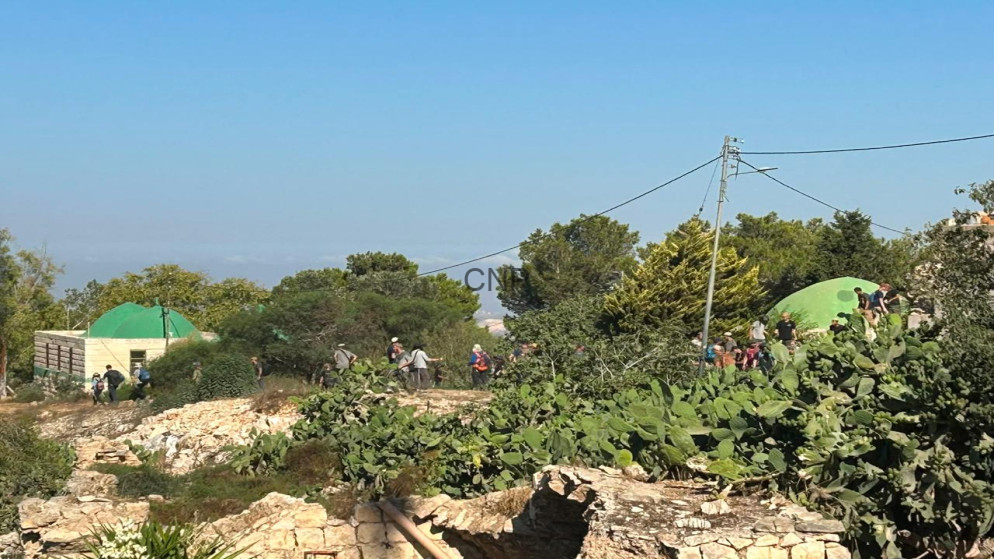 Group of hikers near bright green dome tents on a rocky hillside with cactus and stone walls under a clear blue sky.