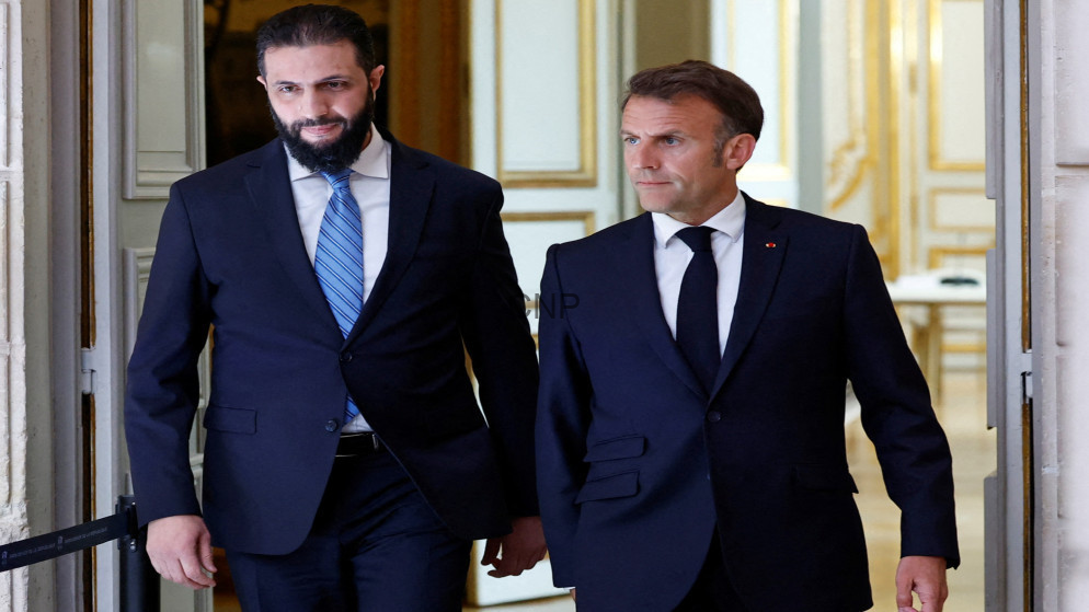 image - Center News Network Two men in dark suits walk out of an ornate doorway, one wearing a blue striped tie, the other with a black tie, looking ahead.