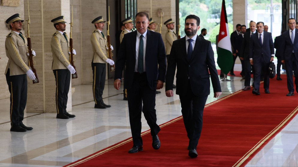 image - Center News Network Two men in suits walk on a red carpet during a formal welcome, flanked by guards with rifles; a flag is visible in the background.