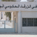 Facade of the New Zarqa Government Hospital with gated entrance, Arabic sign (مستشفى الزرقاء الحكومي الجديد) atop the building.