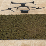 Quadcopter drone hovering above a large sheet of dried cannabis laid out on a tarp on a tiled surface to document the harvest/seizure.