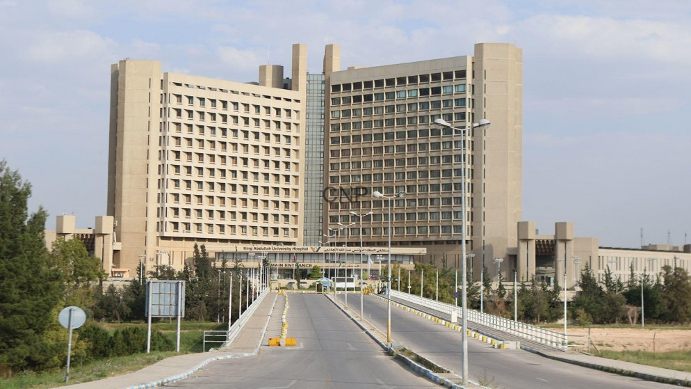 image - Center News Network Front view of a large, multi-wing hospital building seen from a driveway leading to the main entrance with streetlights and landscaping.