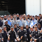 Group of uniformed military personnel posing for a photo in front of a hangar.