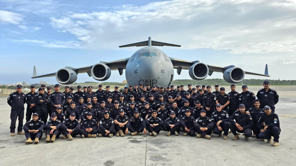 Group of uniformed aircrew posing in front of a four-engine cargo aircraft on the runway with a clear sky above.