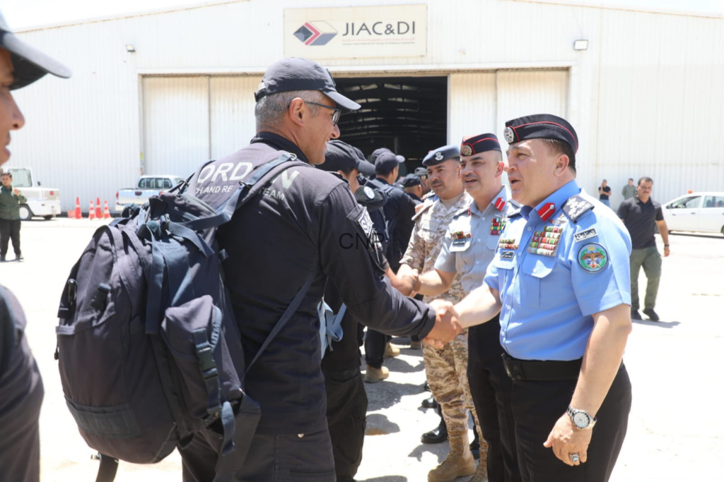 Uniformed military personnel shake hands outside a hangar, with others lined up in the background.
