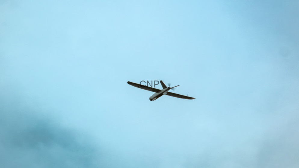 Small propeller airplane seen from below, flying against a pale blue sky.