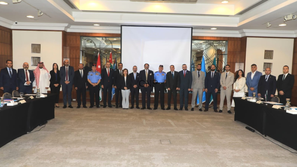 Group of officials and delegates standing in a conference room with flags and a projector screen behind them, posing for a formal photo.