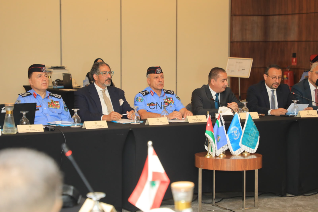 Panel of officials seated at a long table during a formal conference; uniformed officers in blue dress with medals flank suited delegates, microphones and nameplates visible.