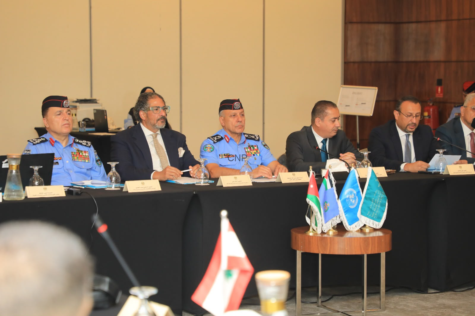 image - Center News Network Panel of officials seated at a long table during a formal conference; uniformed officers in blue dress with medals flank suited delegates, microphones and nameplates visible.