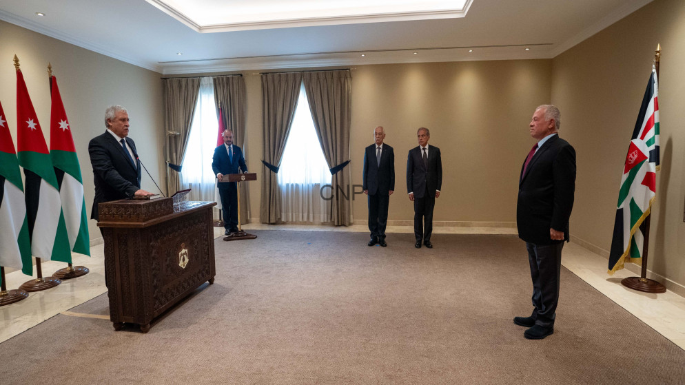 Formal briefing: speaker at an ornately carved podium with Jordan flags on the left; four men in suits observe.