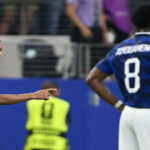 Two soccer players in blue jerseys on a field; one points while facing the other, number 8 visible on the back of the second player.