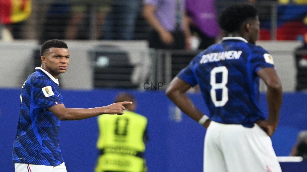 image - Center News Network Two soccer players in blue jerseys on a field; one points while facing the other, number 8 visible on the back of the second player.