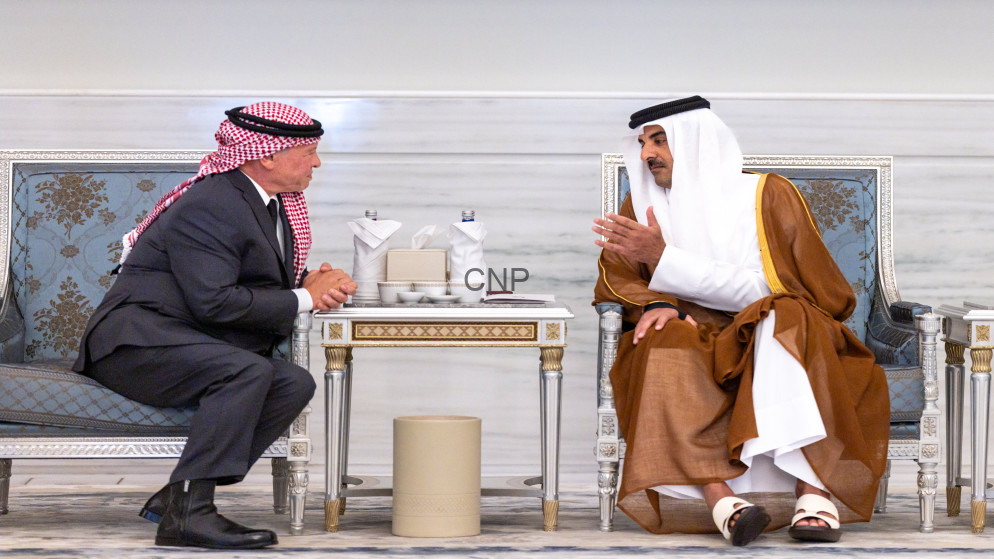 image - Center News Network Two men sit in ornate chairs across a small table, wearing traditional Middle Eastern attire, conversing in a marble-floored room.