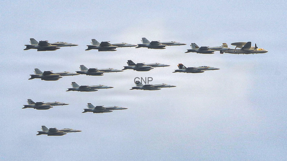 image - Center News Network Twelve fighter jets flying in a tight formation across a clear blue sky, with a larger support aircraft at the far right.