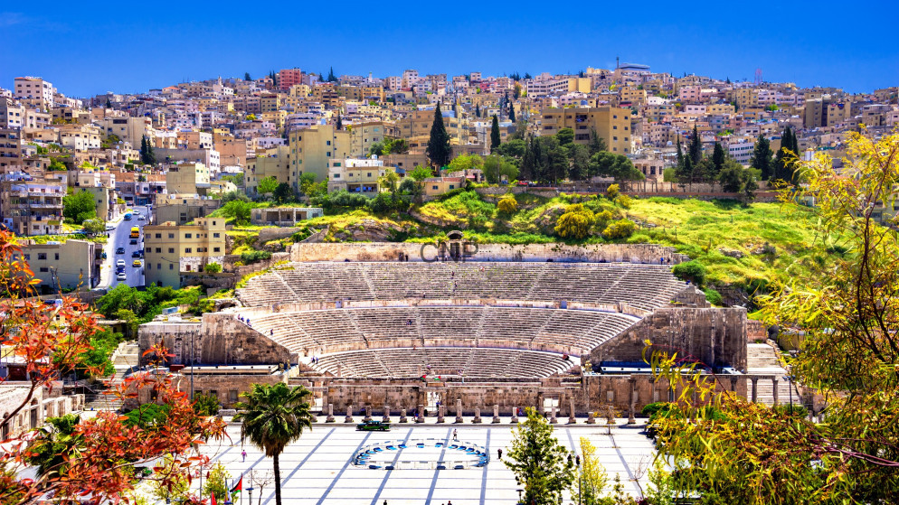Roman amphitheater in Amman, Jordan, with tiered stone seating against a hillside city under a bright blue sky.