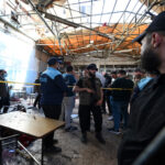 Group of people, including a police officer, in a debris-filled, collapsed building cordoned off with yellow tape.