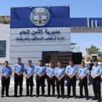 Line of uniformed police officers standing in a row outside a blue-and-white building with Arabic signage and a crest above the entrance.