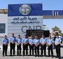 Line of uniformed police officers standing in a row outside a blue-and-white building with Arabic signage and a crest above the entrance.