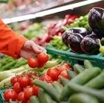 Person selecting fresh vegetables at a market stall, reaching for produce among peppers and tomatoes.