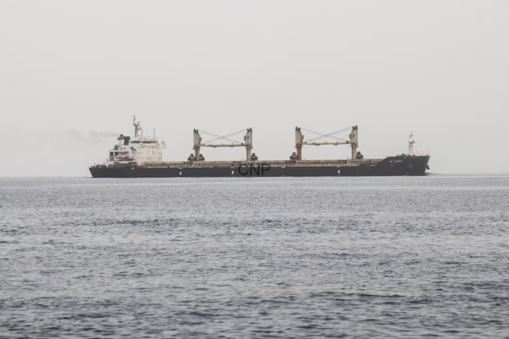 image - Center News Network Large cargo ship with two gantry cranes sailing on a calm, gray sea under a pale sky.
